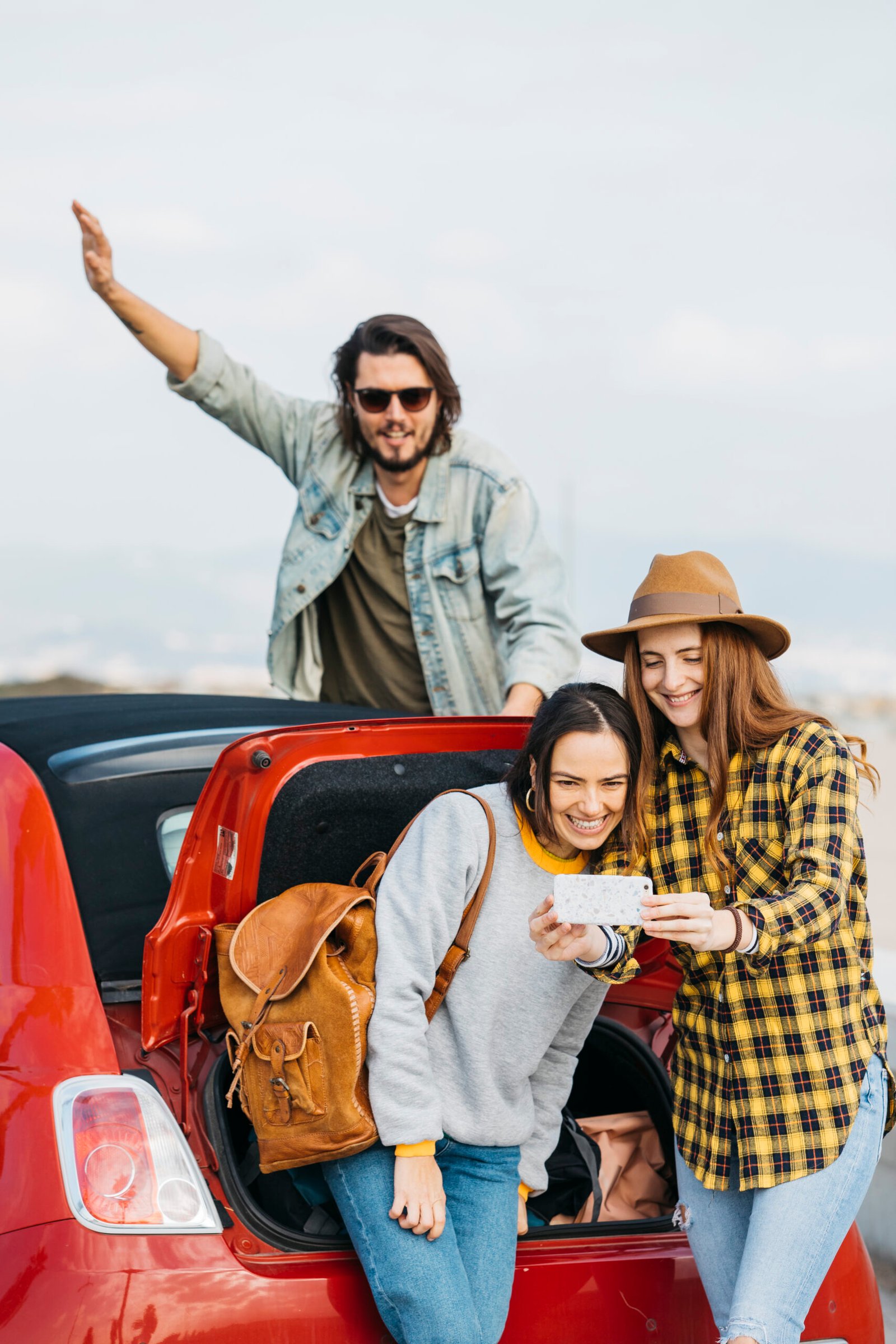 positive-women-taking-selfie-smartphone-near-car-trunk-man-leaning-out-from-auto